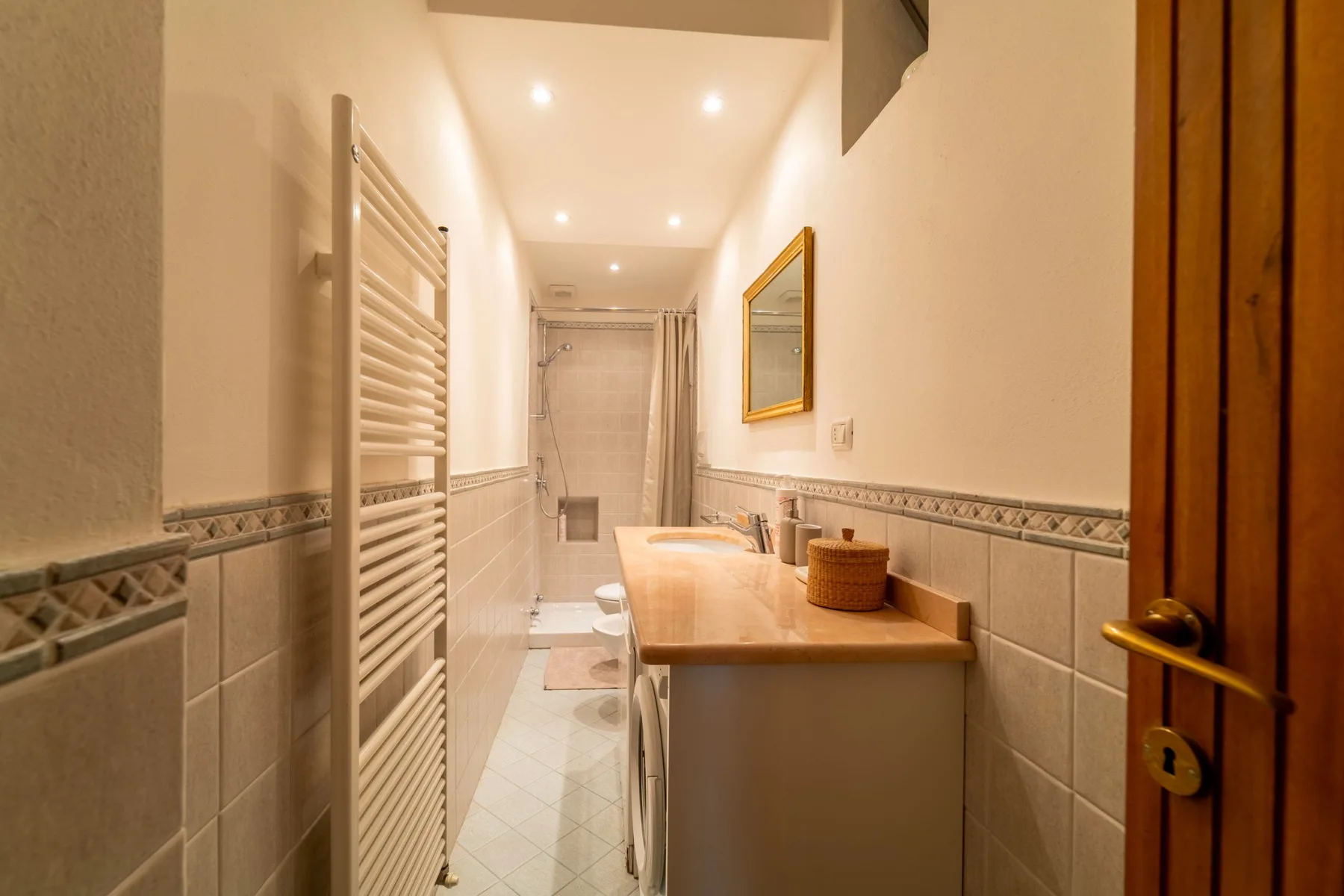 A bright bathroom with a long vanity and a shower at the far end.