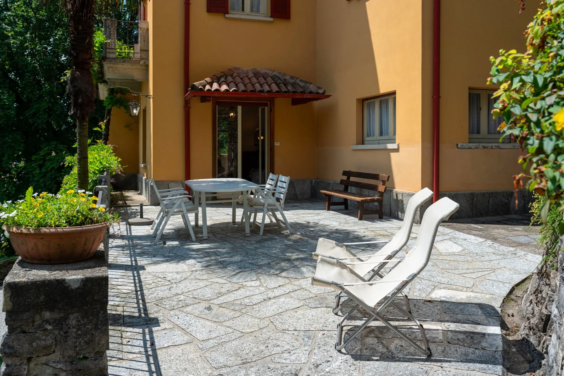 A sunny outdoor patio with seating, a table, and a yellow building.