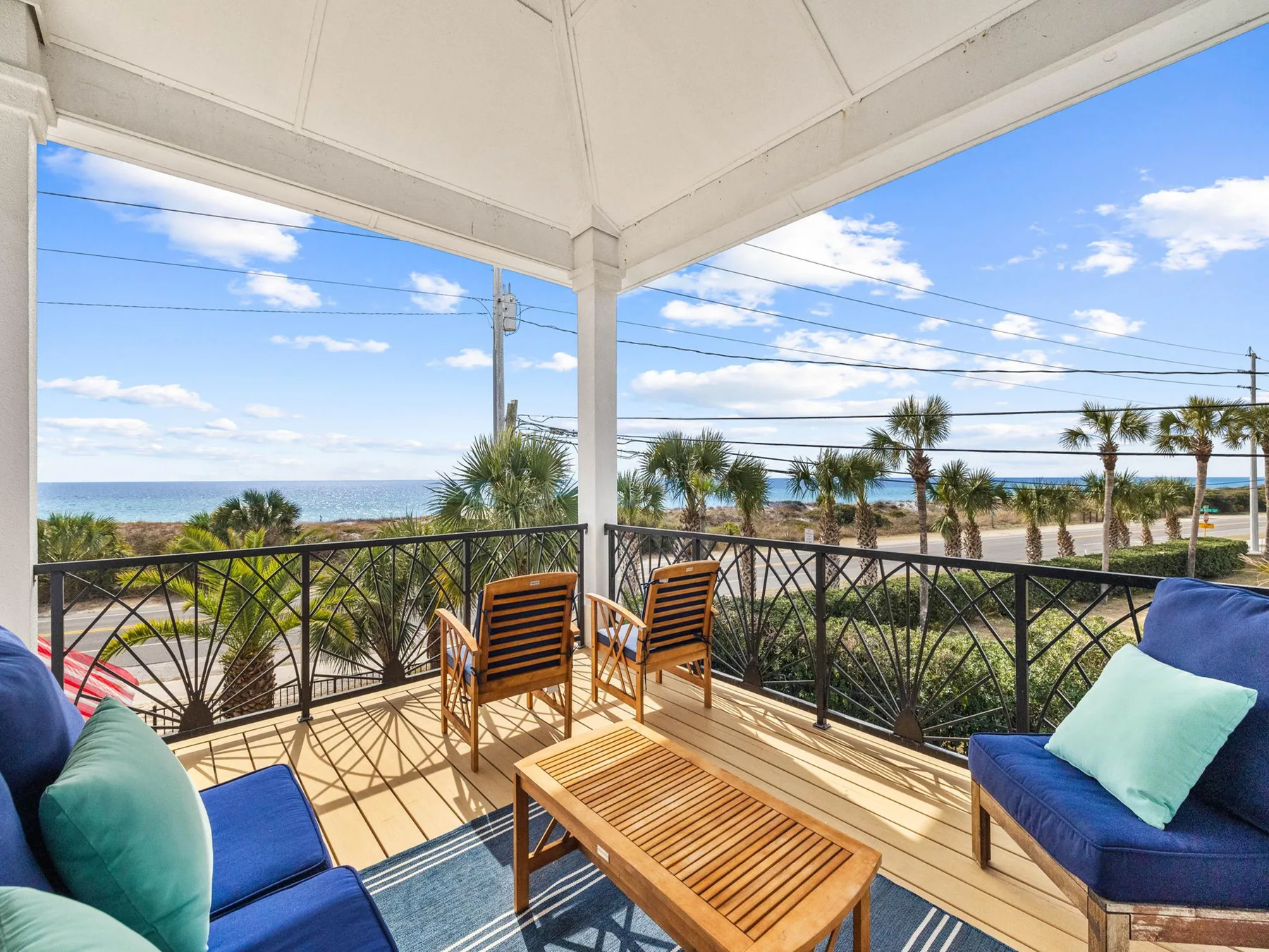 A covered balcony seating area overlooks palm trees and the ocean.