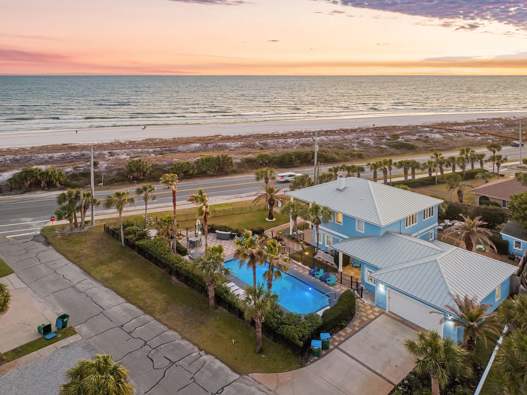 A coastal house and pool sit beside a road, with the ocean visible beyond the beach.