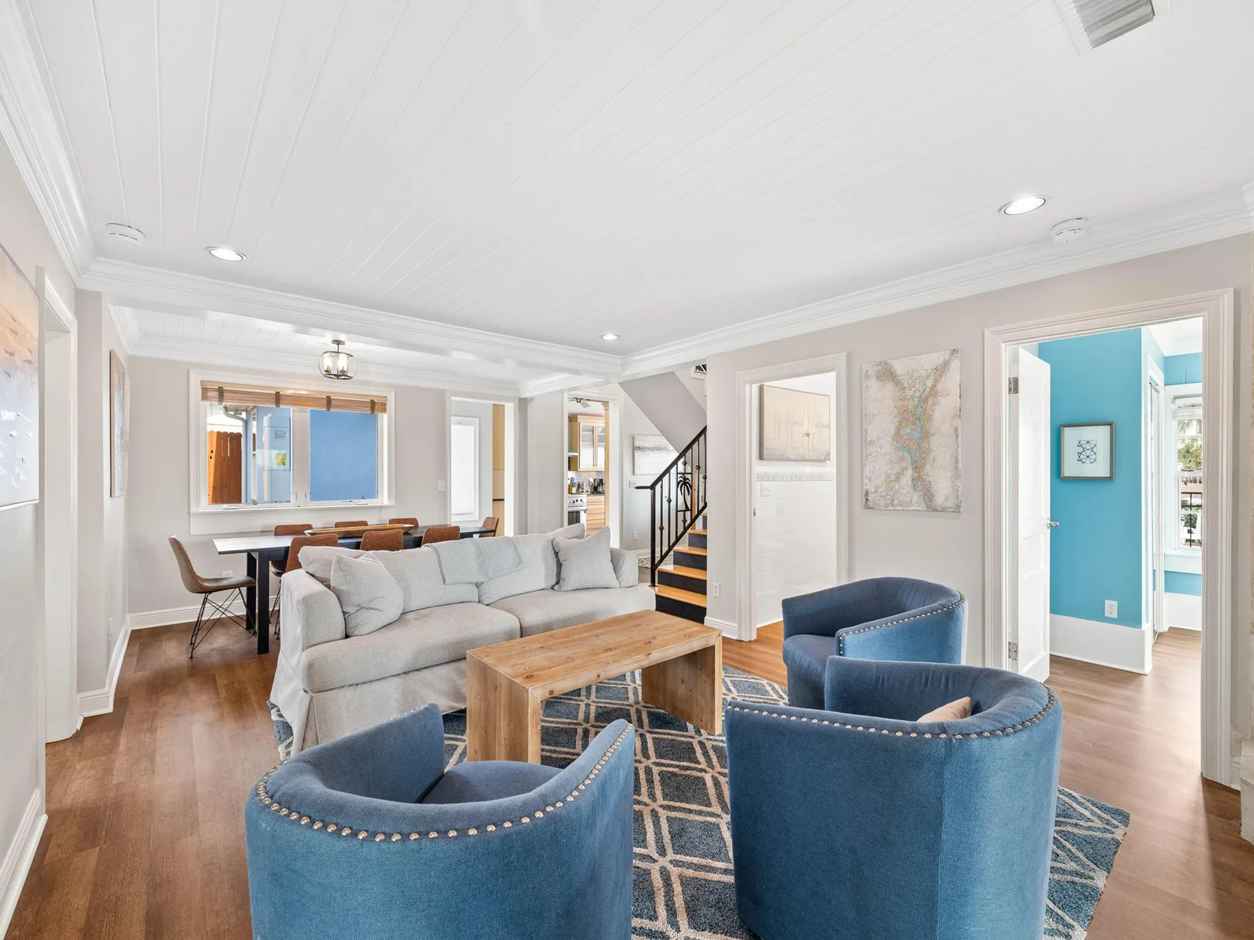 A bright living room has blue seating, a pale sofa, and a wooden coffee table.