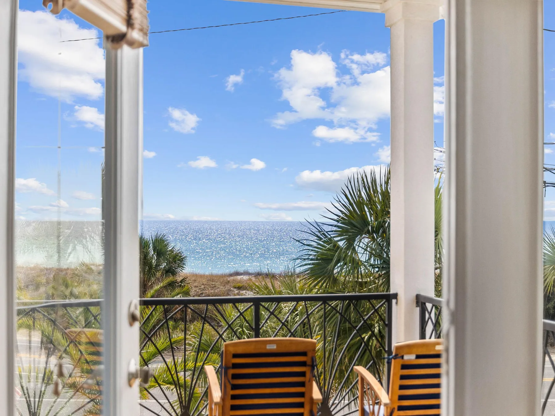 A balcony overlooks the ocean, with two striped chairs beside the railing.