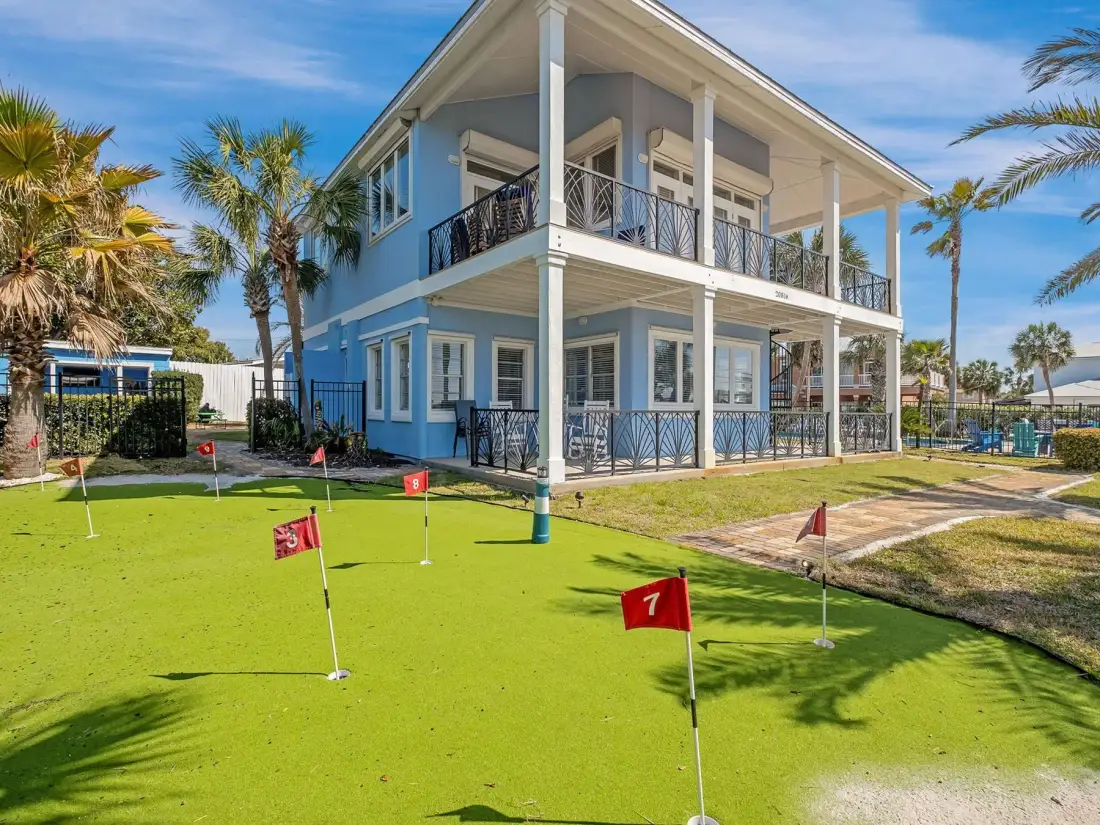 A two-story building overlooks a green putting area with several flag markers.