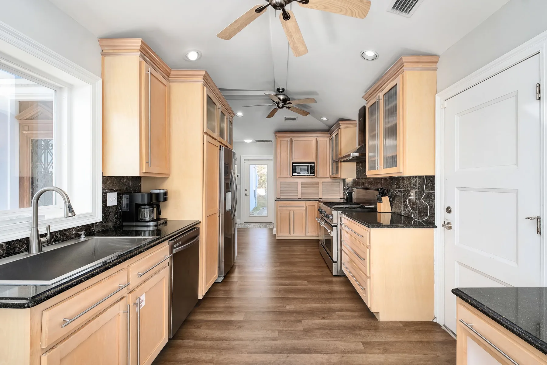 A spacious kitchen with light wood cabinetry, dark counters, and a central aisle.