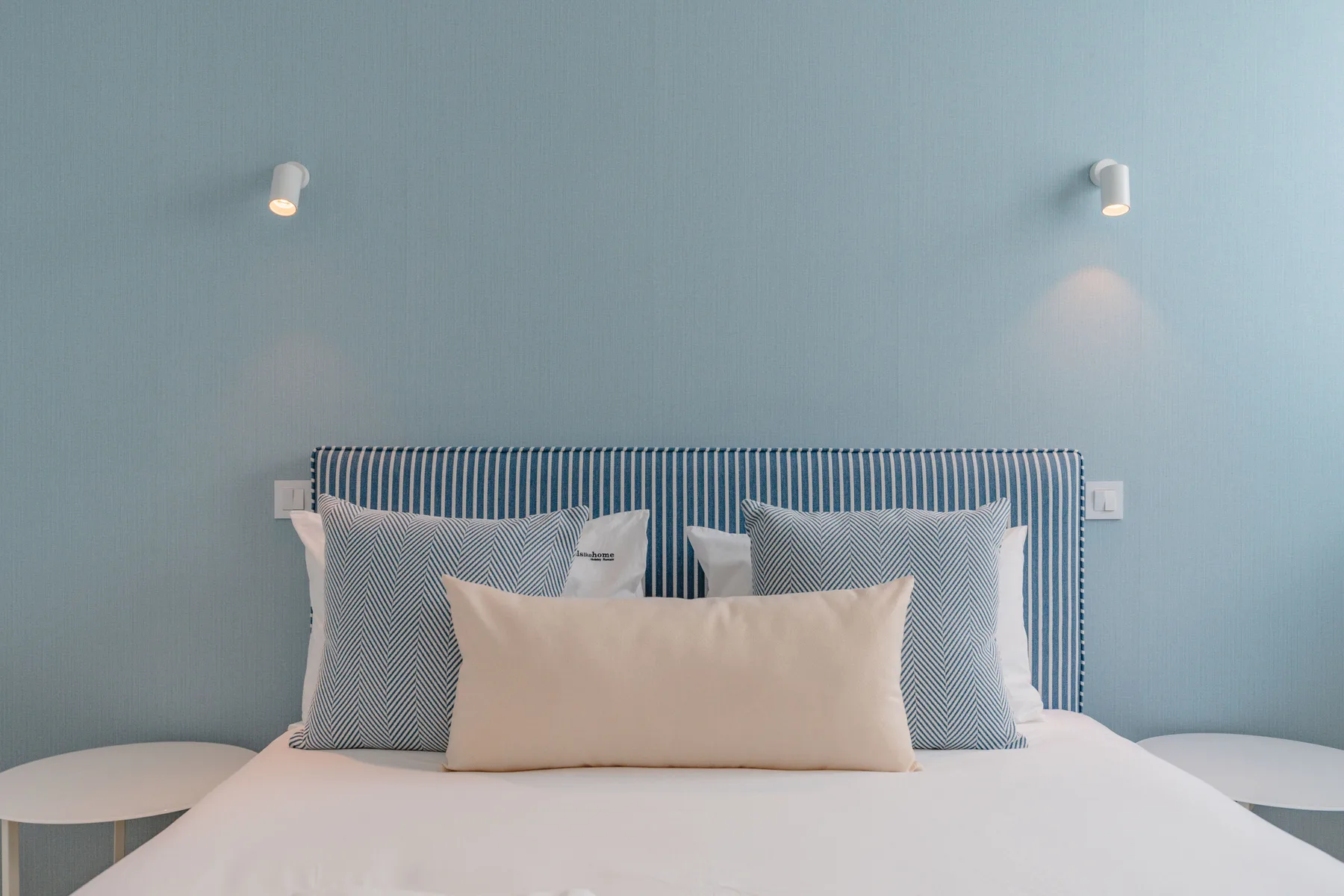 Un dormitorio con una cama bien tendida junto a una pared azul.