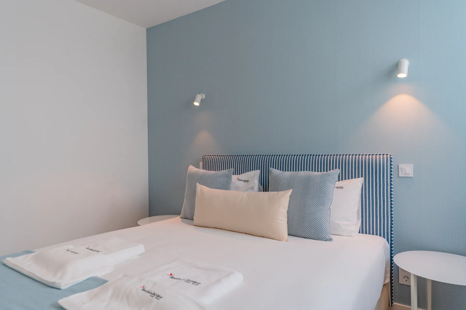 Un dormitorio con una cama bien tendida junto a una pared azul.