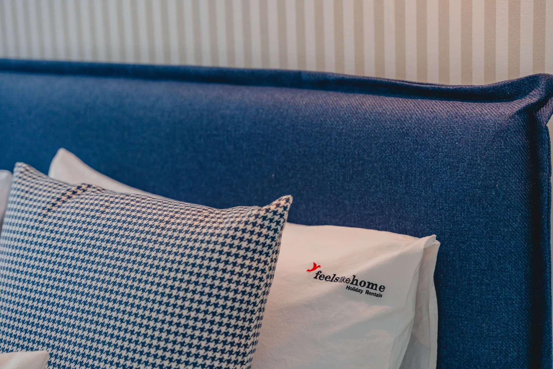 Escena de dormitorio con cabecero azul tapizado y almohadas estampadas.