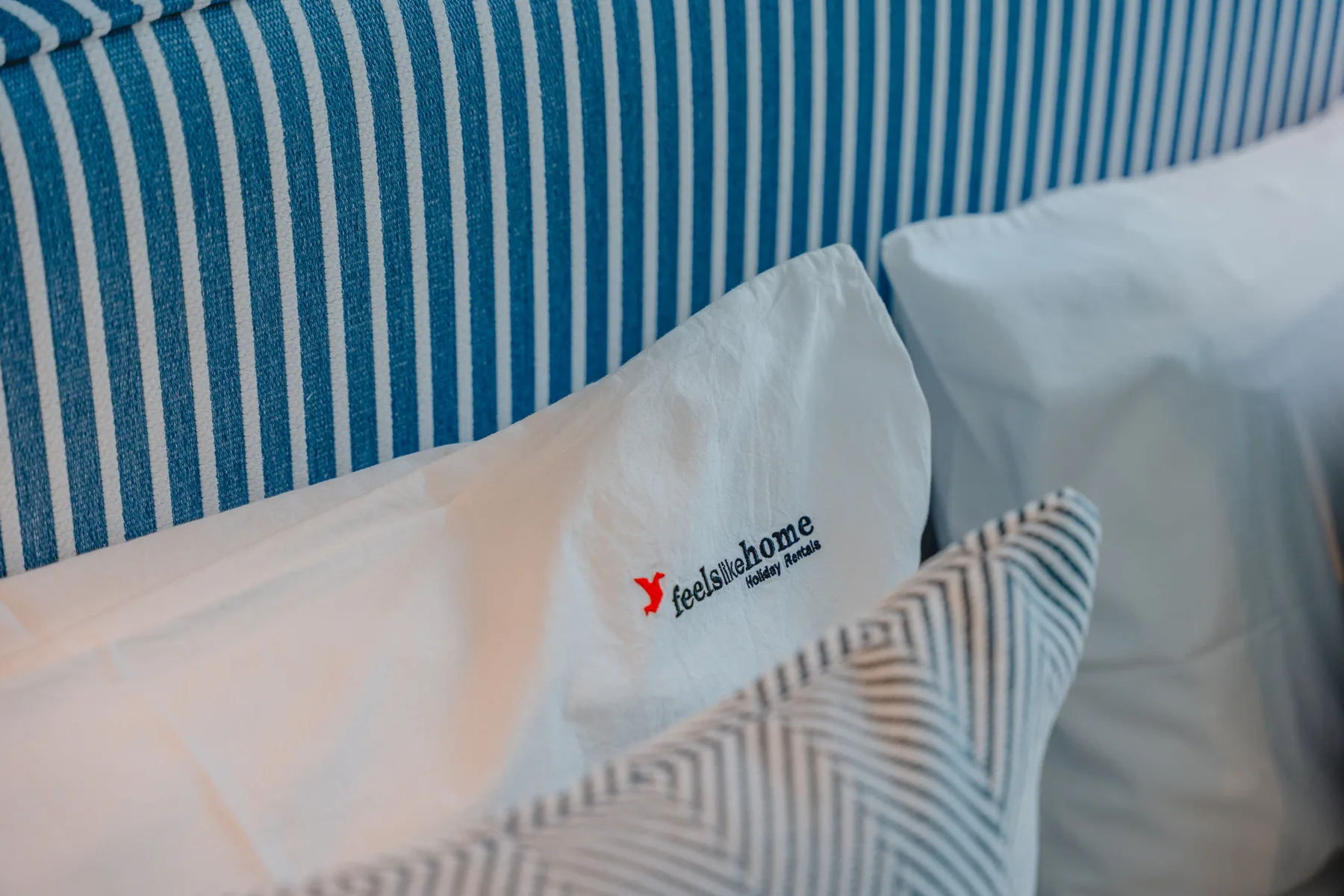 Una cama con almohadas blancas está junto a un cabecero de rayas azules y blancas.