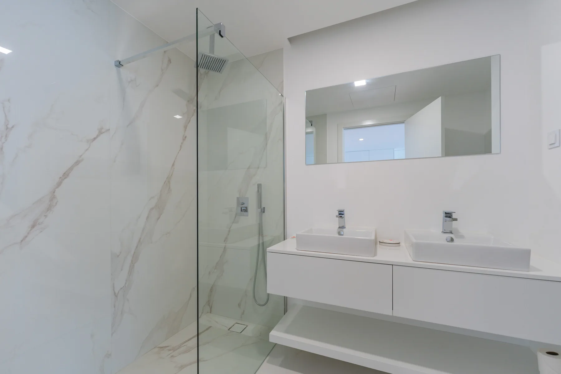 Un baño luminoso con ducha de vidrio y un lavabo doble.
