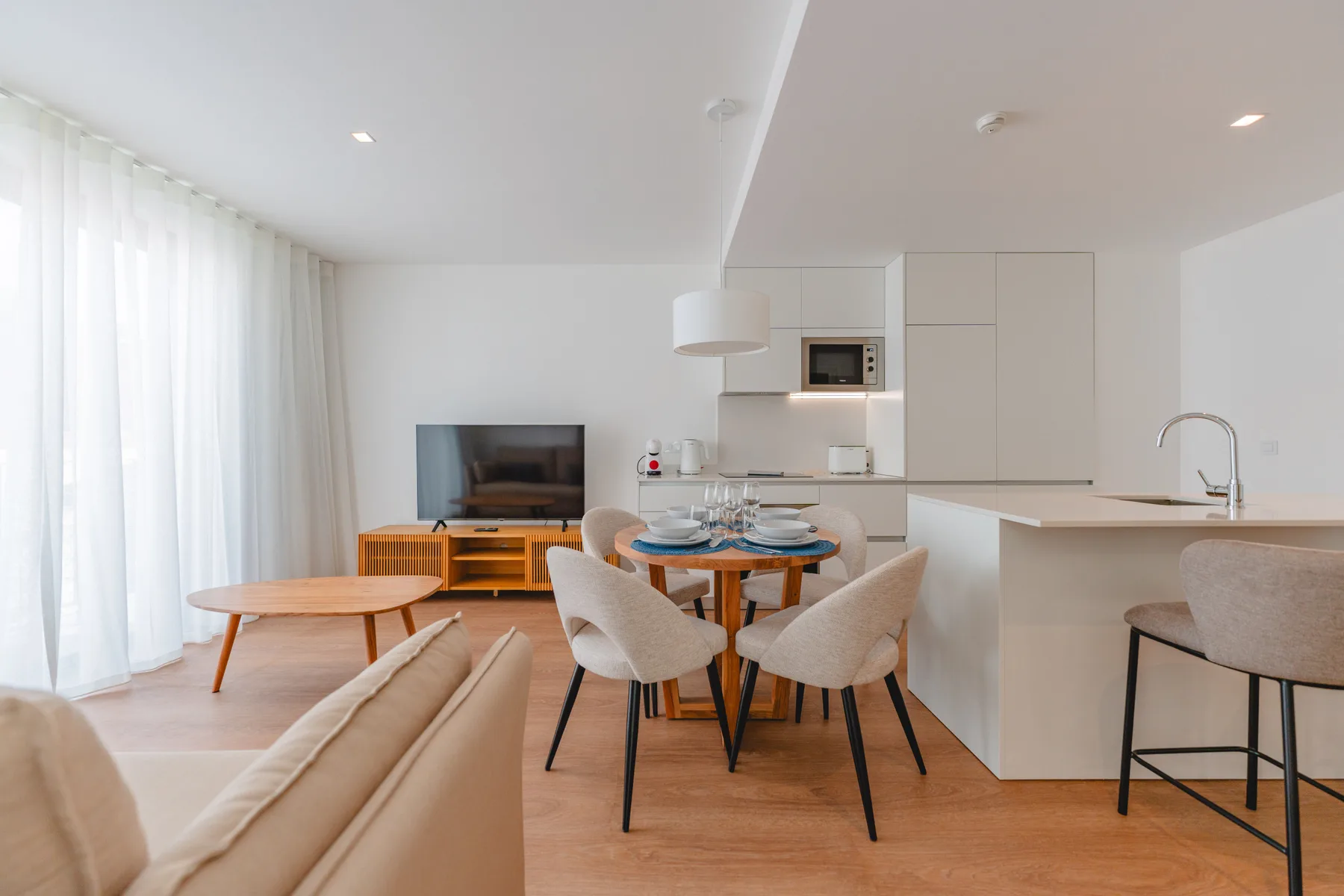 Una luminosa sala de estar y comedor de planta abierta con cocina y ventanales.