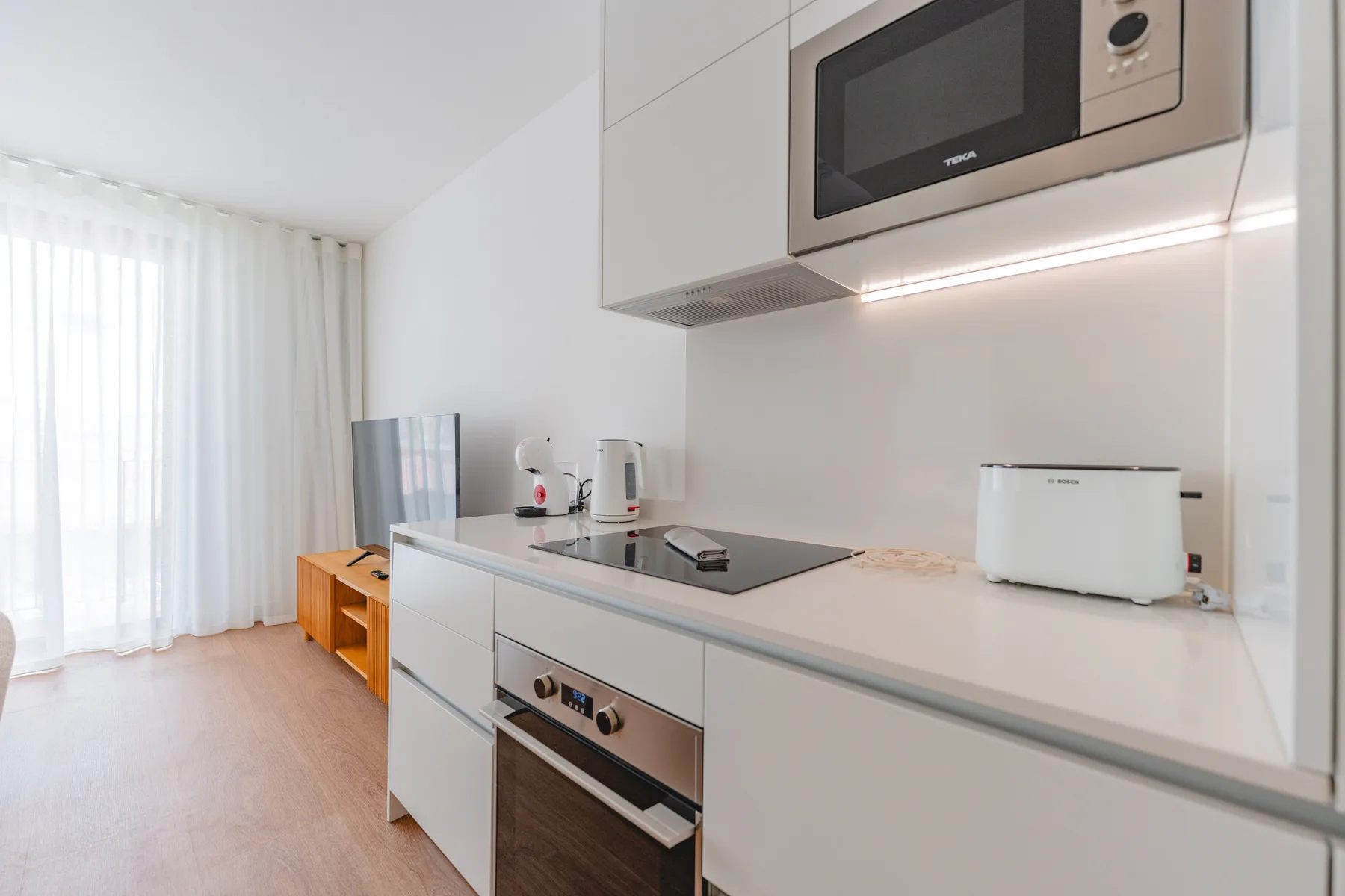 Una cocina luminosa con placa de cocción y horno empotrado junto a ventanas con cortinas.