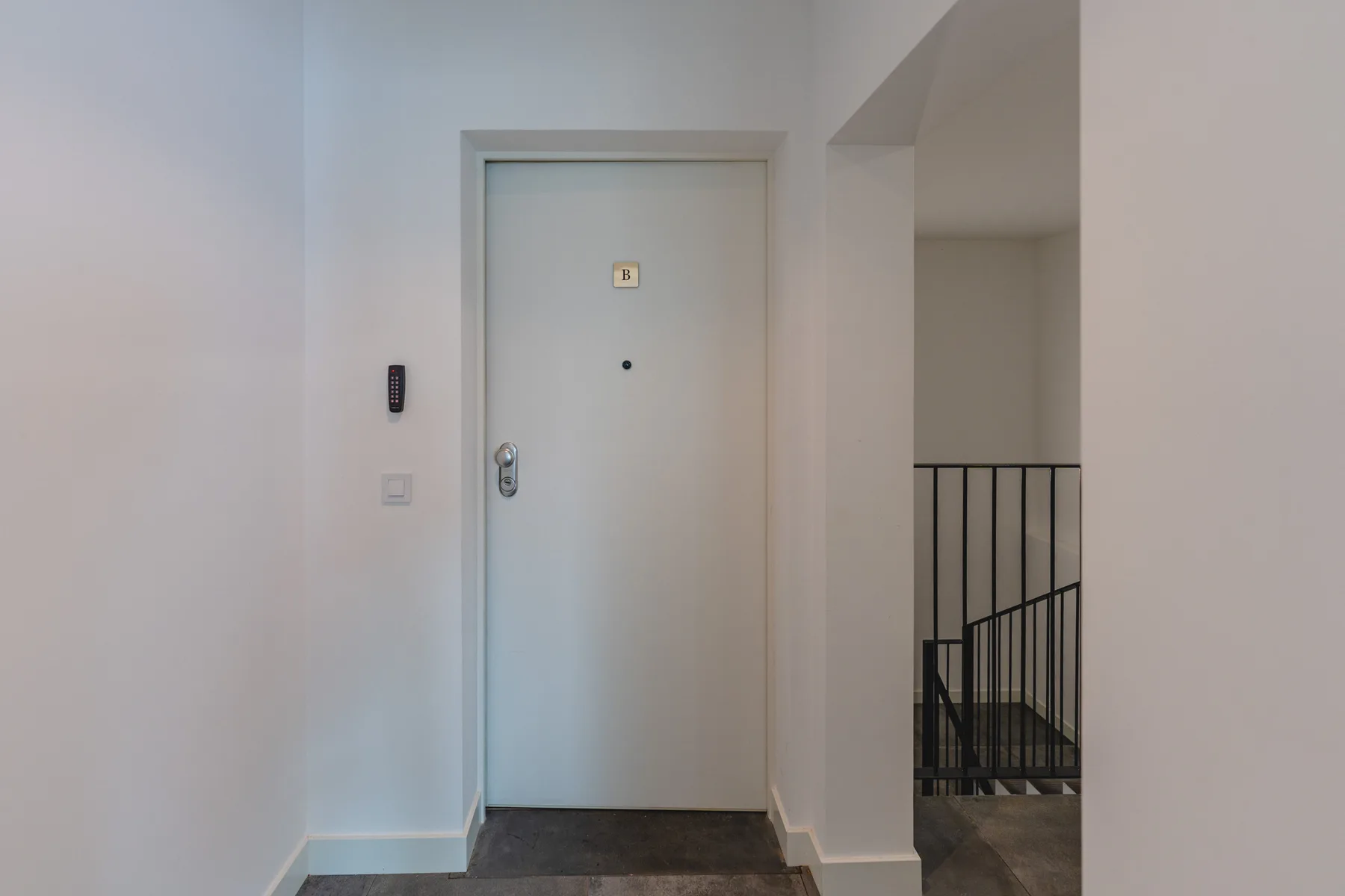 La entrada de un apartamento con una puerta clara junto a una barandilla de escalera.