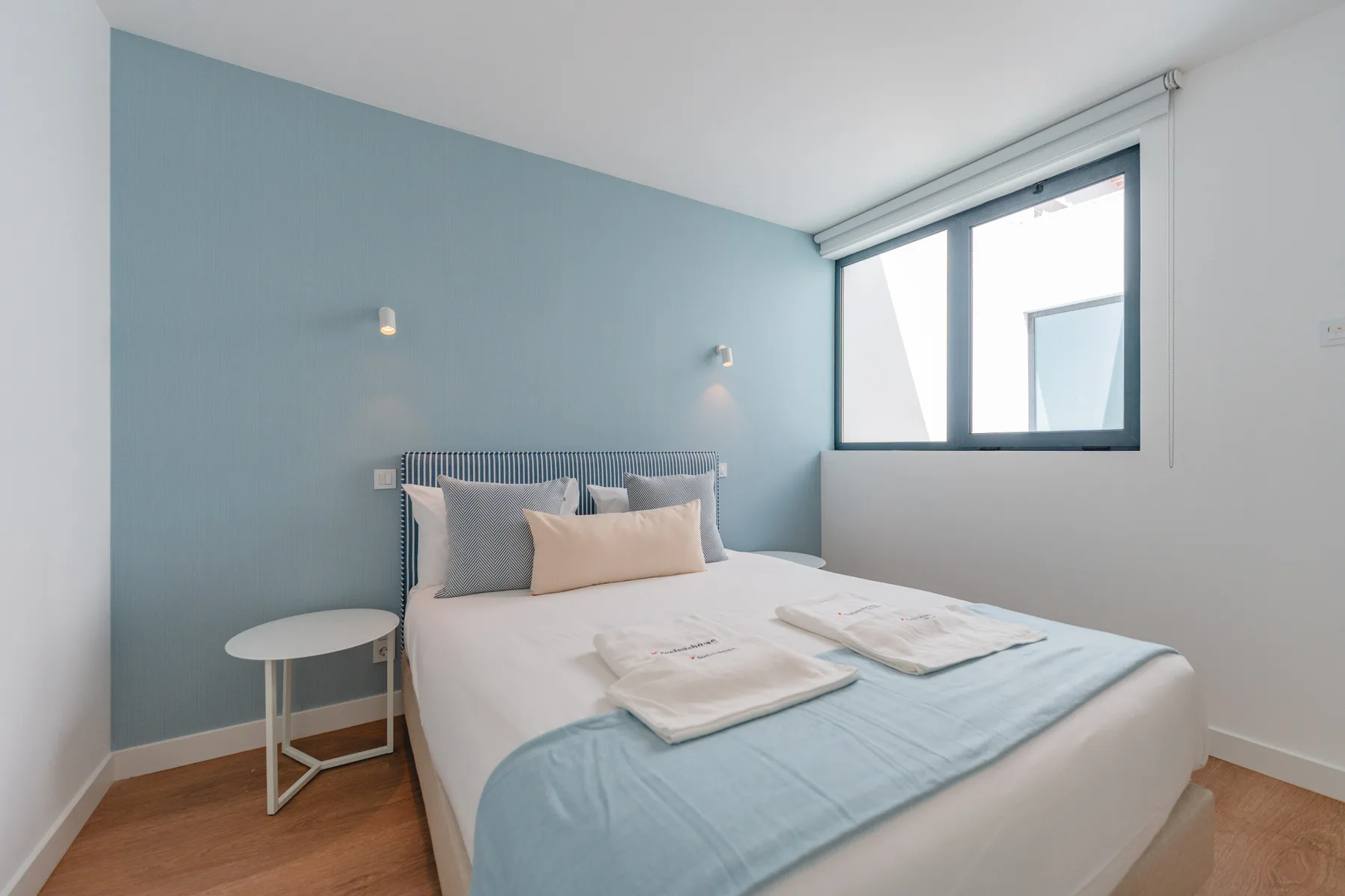 Un dormitorio luminoso con una cama vestida con ropa de cama blanca y azul claro.