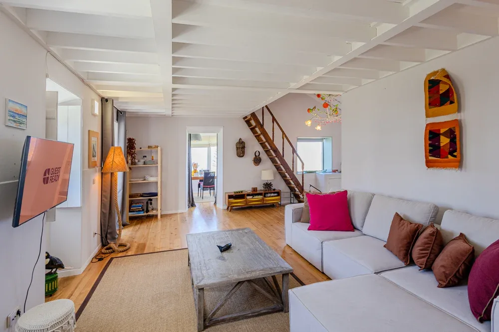 A bright living room with sectional seating, a coffee table, and a staircase.