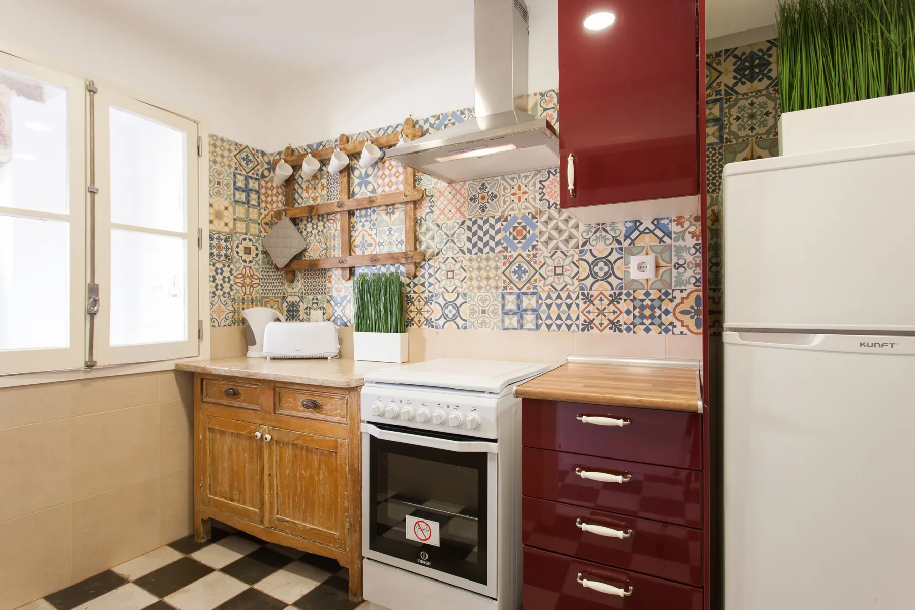 Una cocina con estufa, armarios de madera y azulejos decorados en la pared.