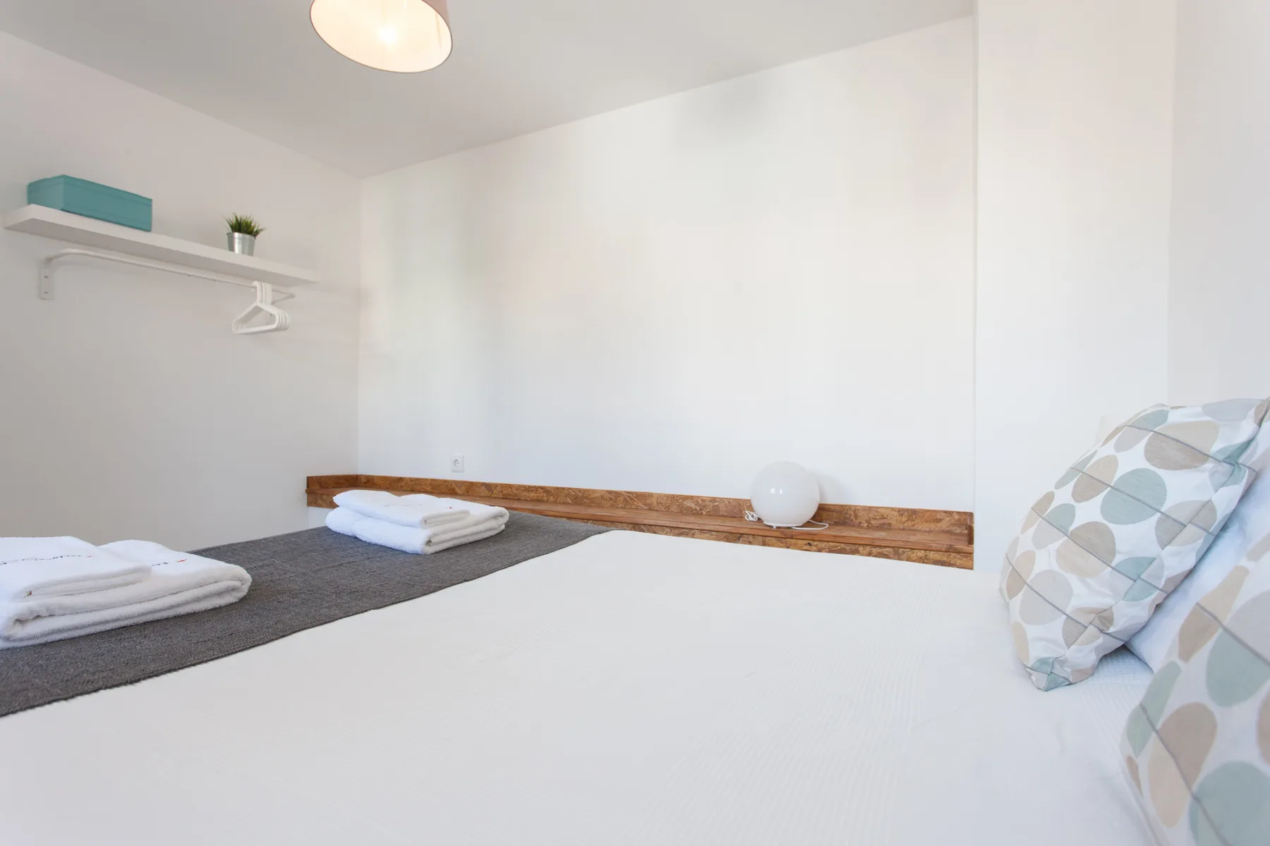 Un dormitorio luminoso con ropa de cama blanca y toallas dobladas sobre la cama.
