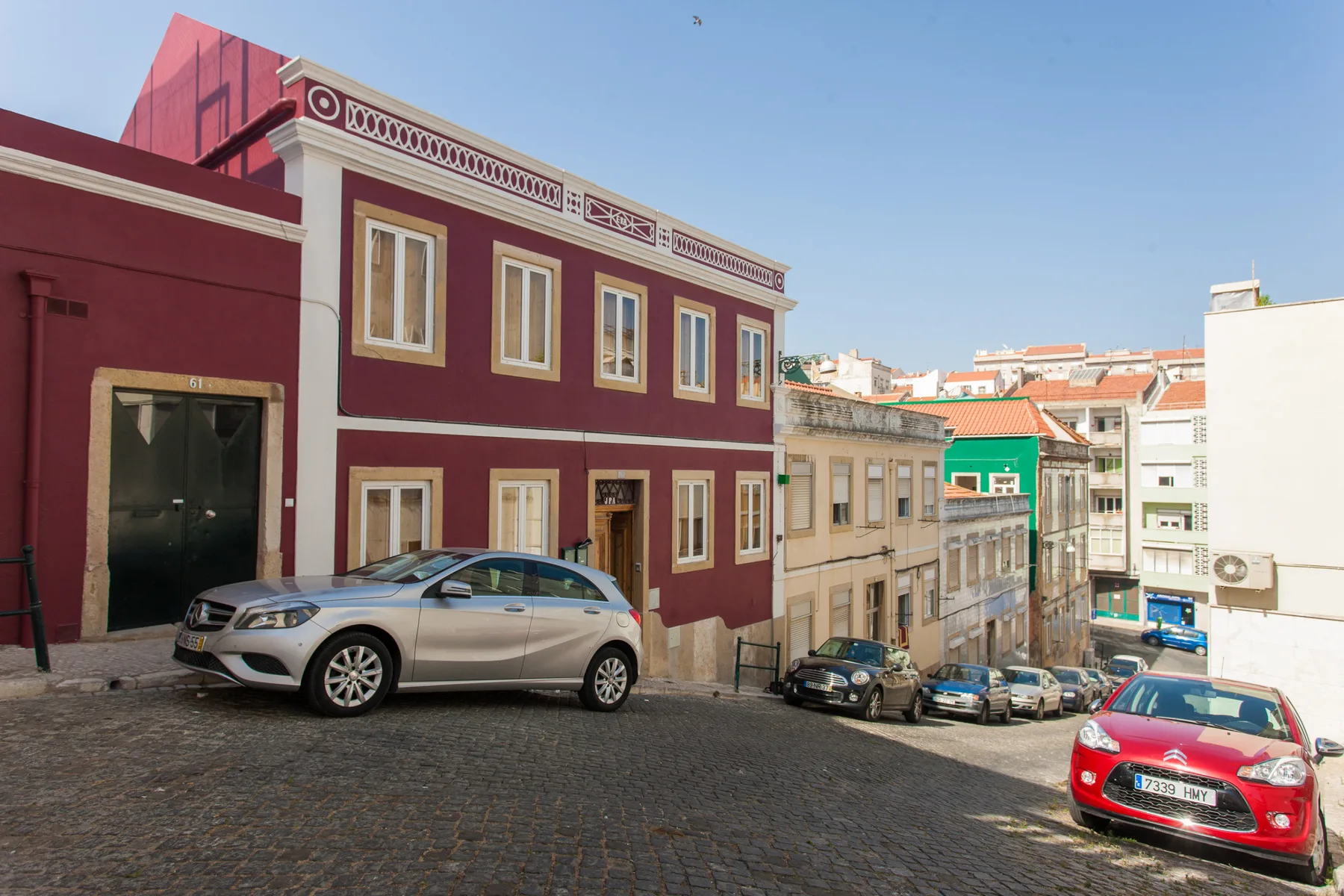 Una calle empedrada desciende junto a edificios coloridos y coches estacionados bajo un cielo despejado.