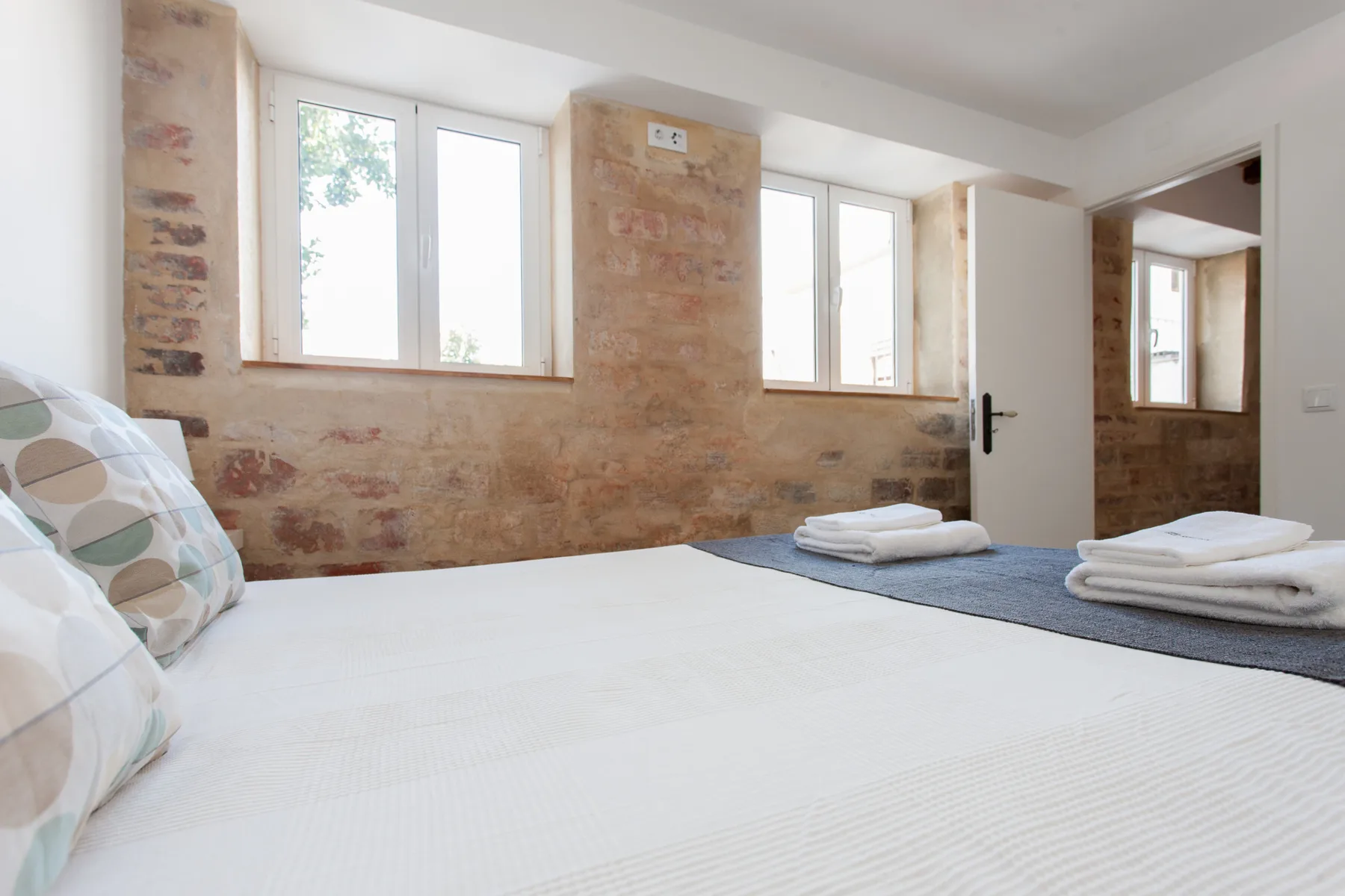 Un dormitorio luminoso con una cama grande, paredes de ladrillo visto y toallas dobladas.