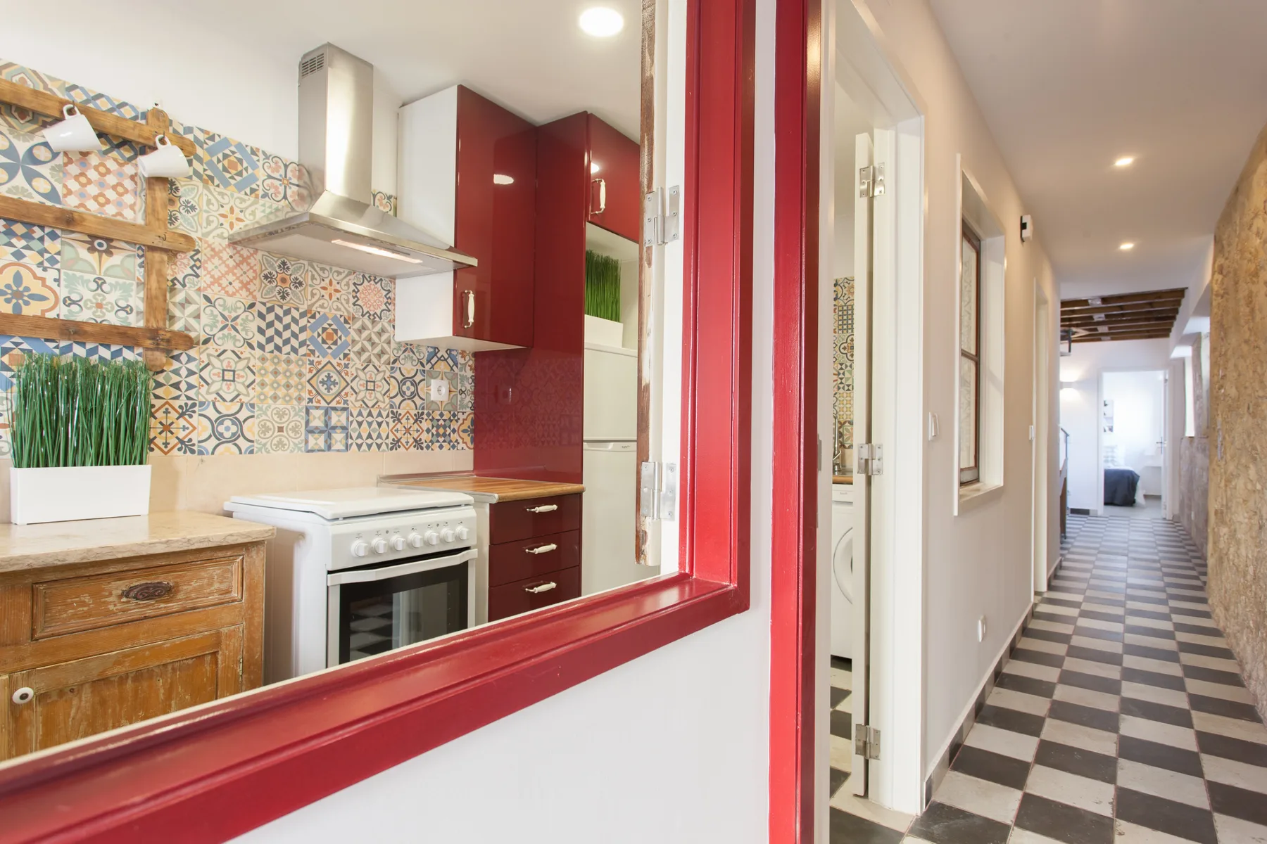 Una cocina con azulejos estampados y un pasillo visible a través de una abertura con marco rojo.