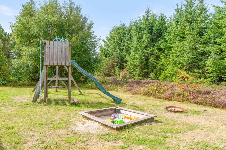 Una pequeña zona de juegos al aire libre con estructura de madera, tobogán y arenero.