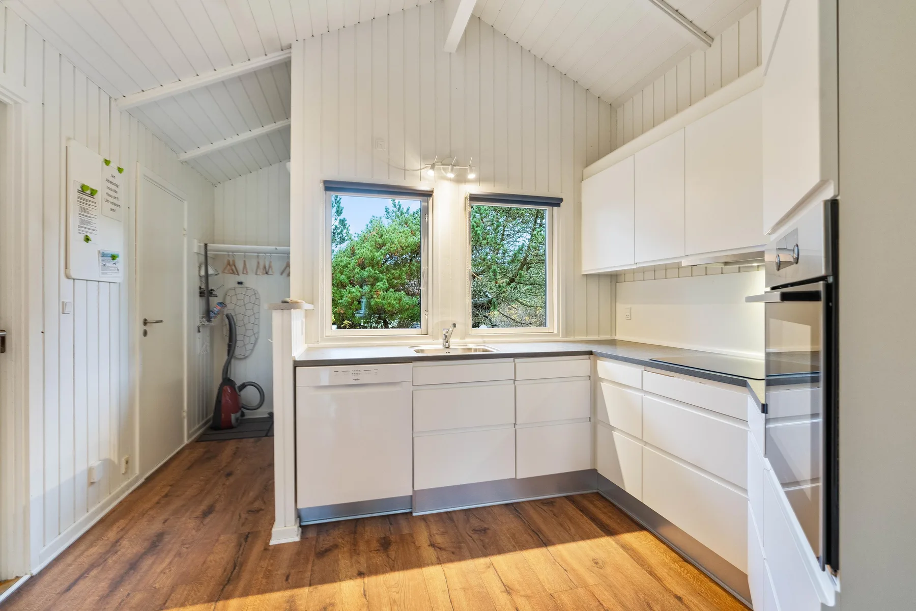 Una cocina luminosa con armarios blancos, encimera y ventanas con vistas a la vegetación.