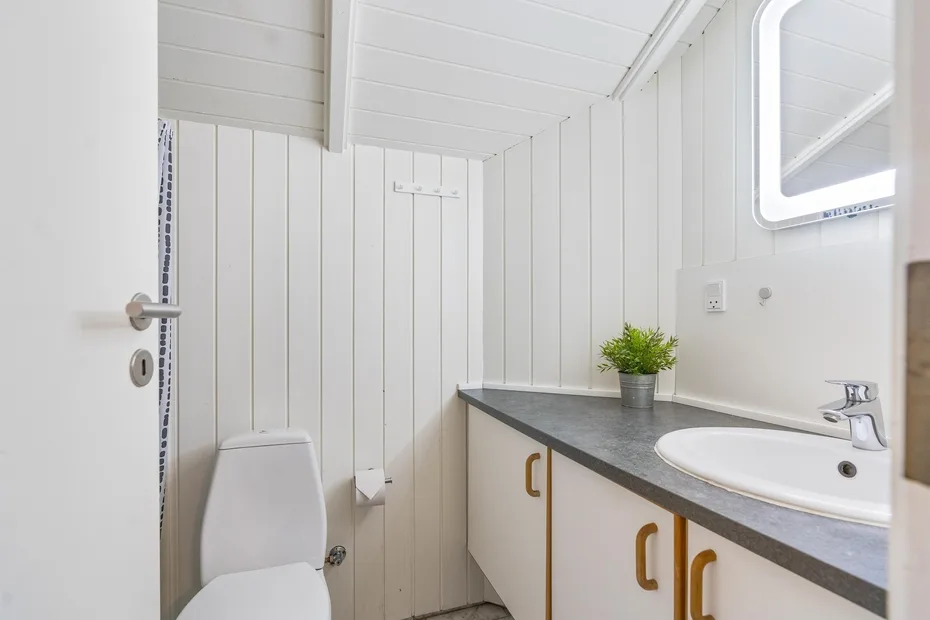 Un baño luminoso con un inodoro blanco y un lavabo bajo un espejo.