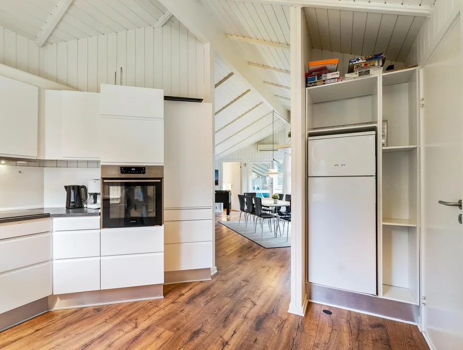 Una cocina luminosa se abre a un comedor bajo un techo blanco inclinado.