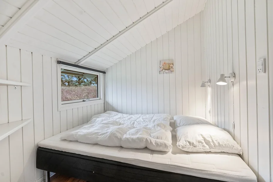 Un dormitorio con una cama bajo un techo inclinado de paneles blancos.