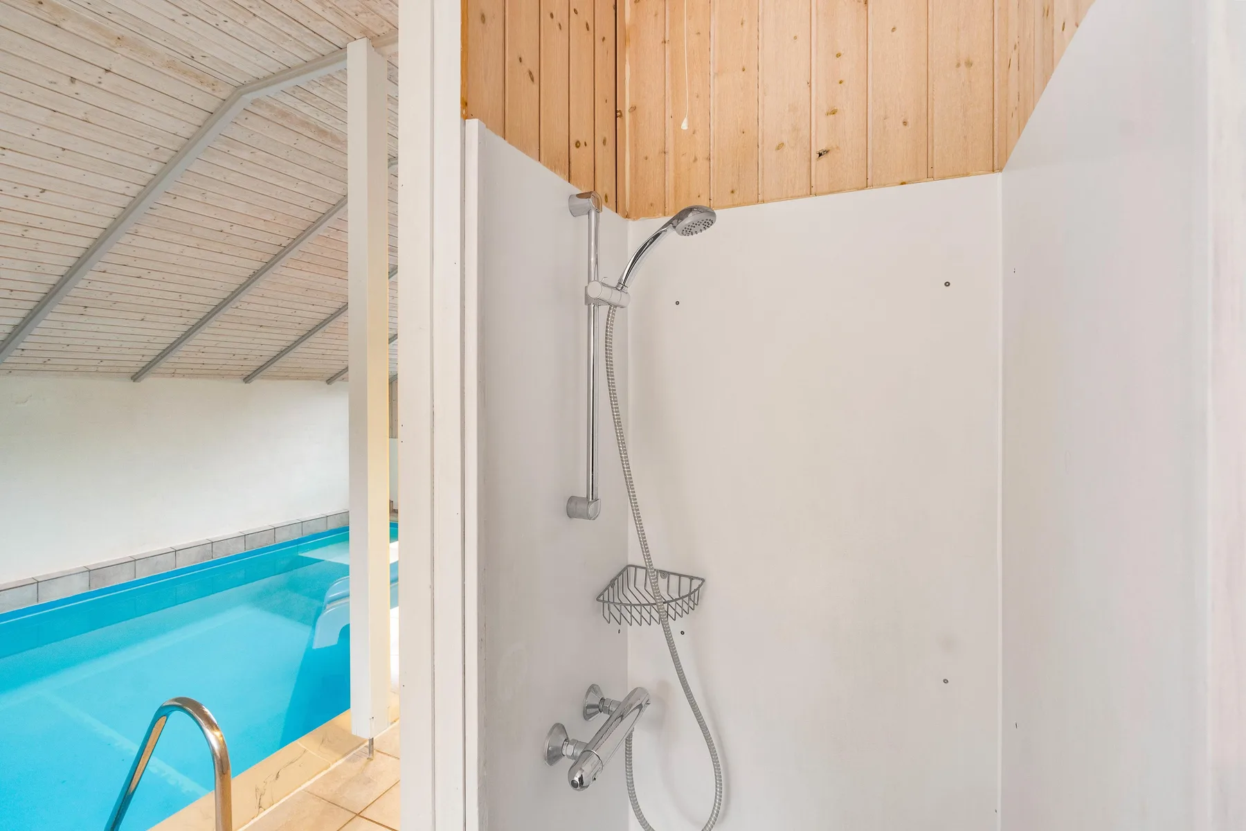 Una zona de ducha con techo de madera da a una piscina cubierta.