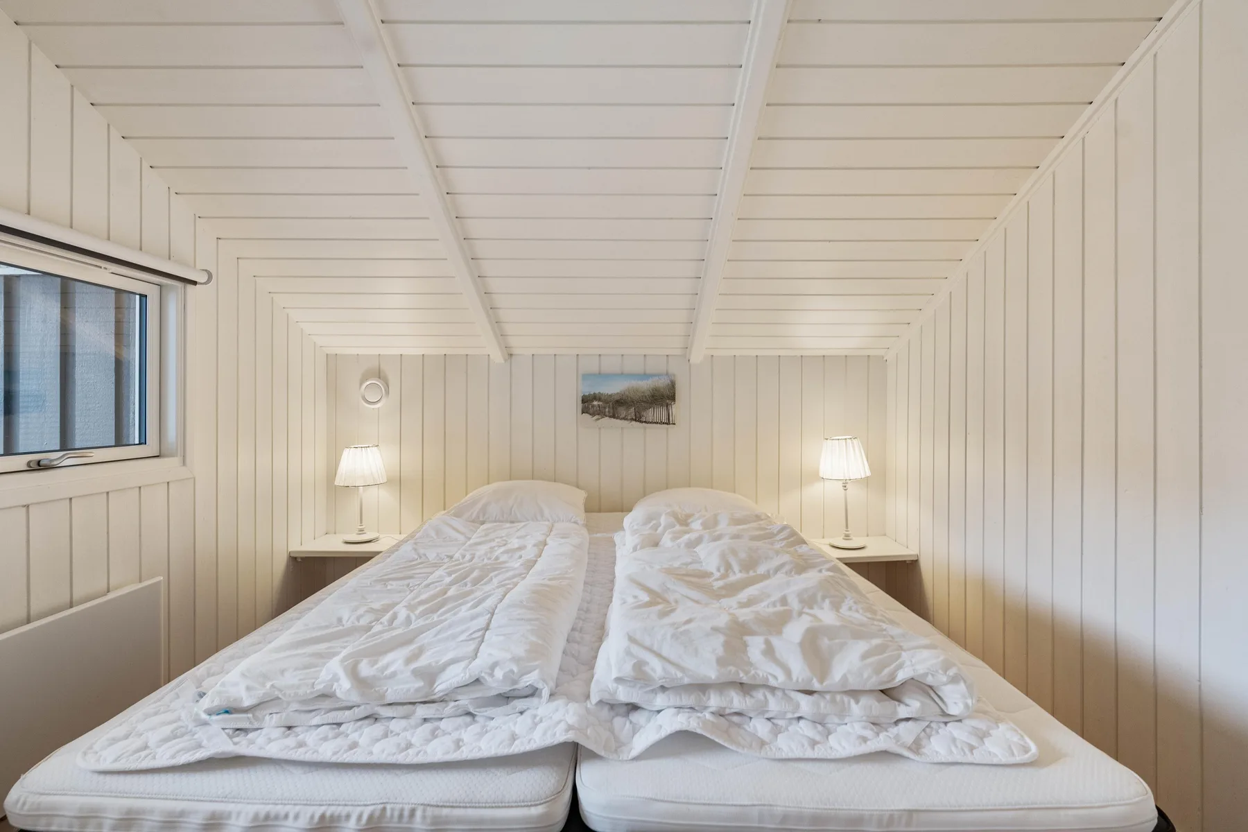 Un dormitorio luminoso con dos camas bajo un techo blanco con paneles.