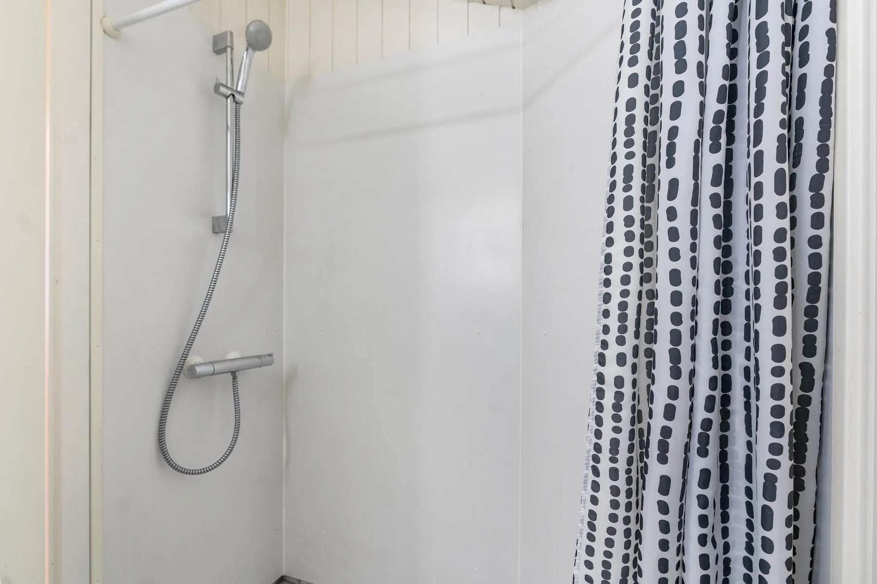 Una zona de ducha con ducha de mano y cortina estampada.