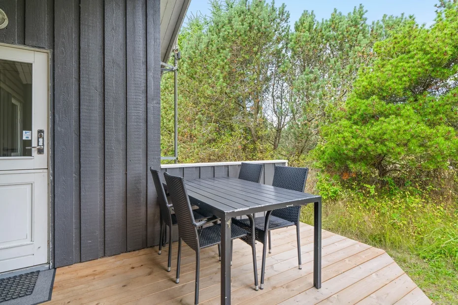 Una terraza exterior tiene una mesa de comedor y asientos junto a árboles frondosos.