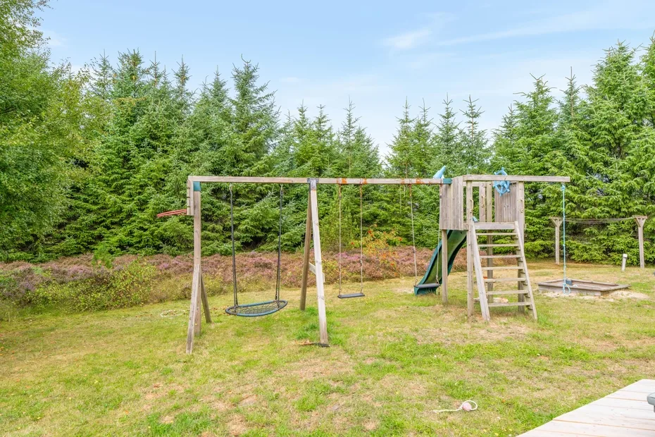 Zona de juegos al aire libre con una estructura de madera y columpios entre árboles.
