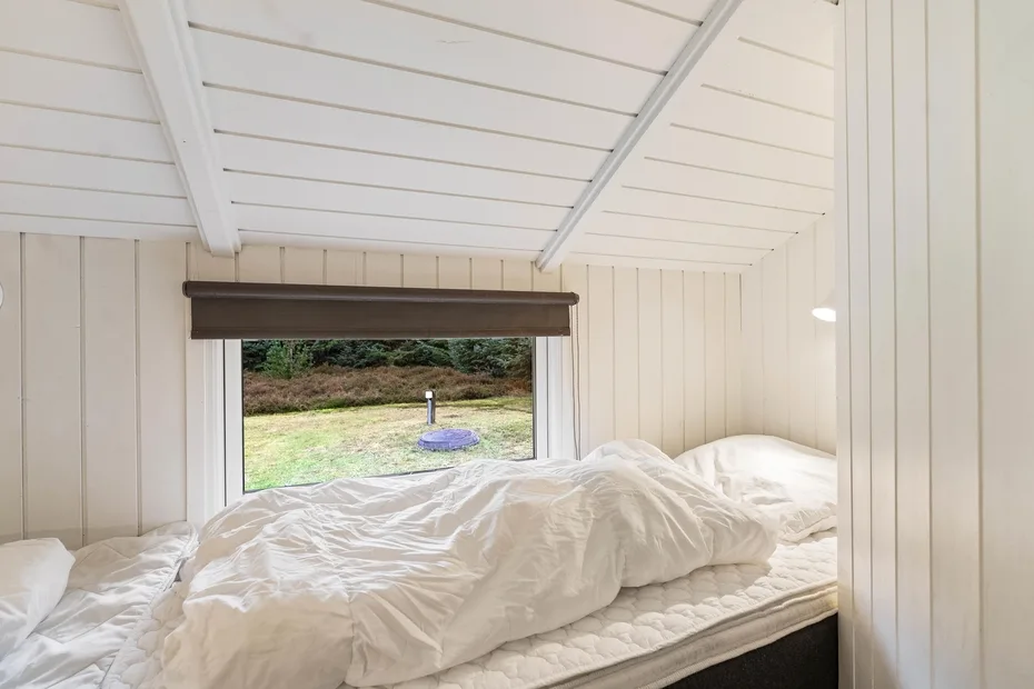 Una cama bajo un techo blanco inclinado da a una zona exterior cubierta de césped.