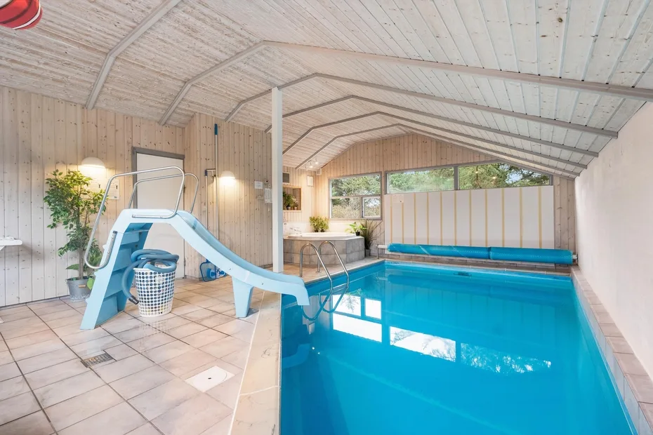 Una piscina cubierta con un tobogán azul y una terraza de baldosas.