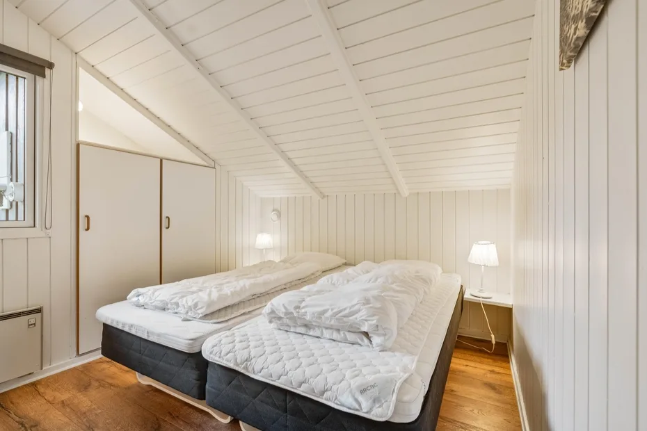 Un dormitorio abuhardillado luminoso con dos camas bajo un techo inclinado.