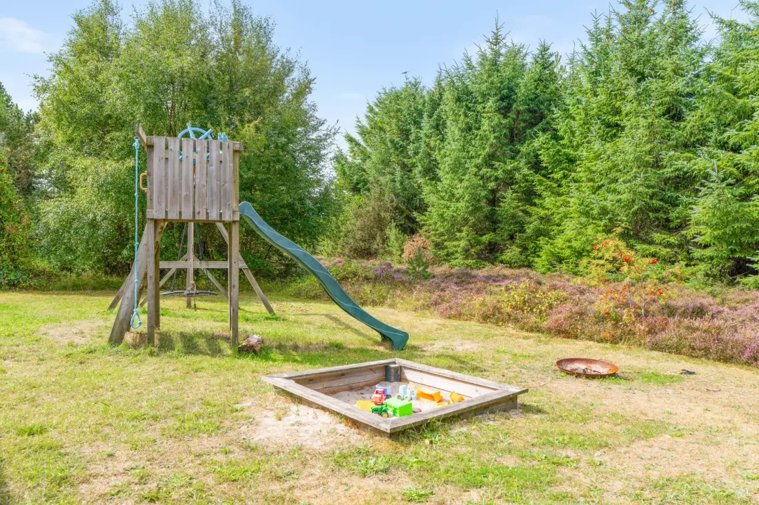 Una zona de juegos al aire libre tiene una estructura de madera, un tobogán y un arenero.