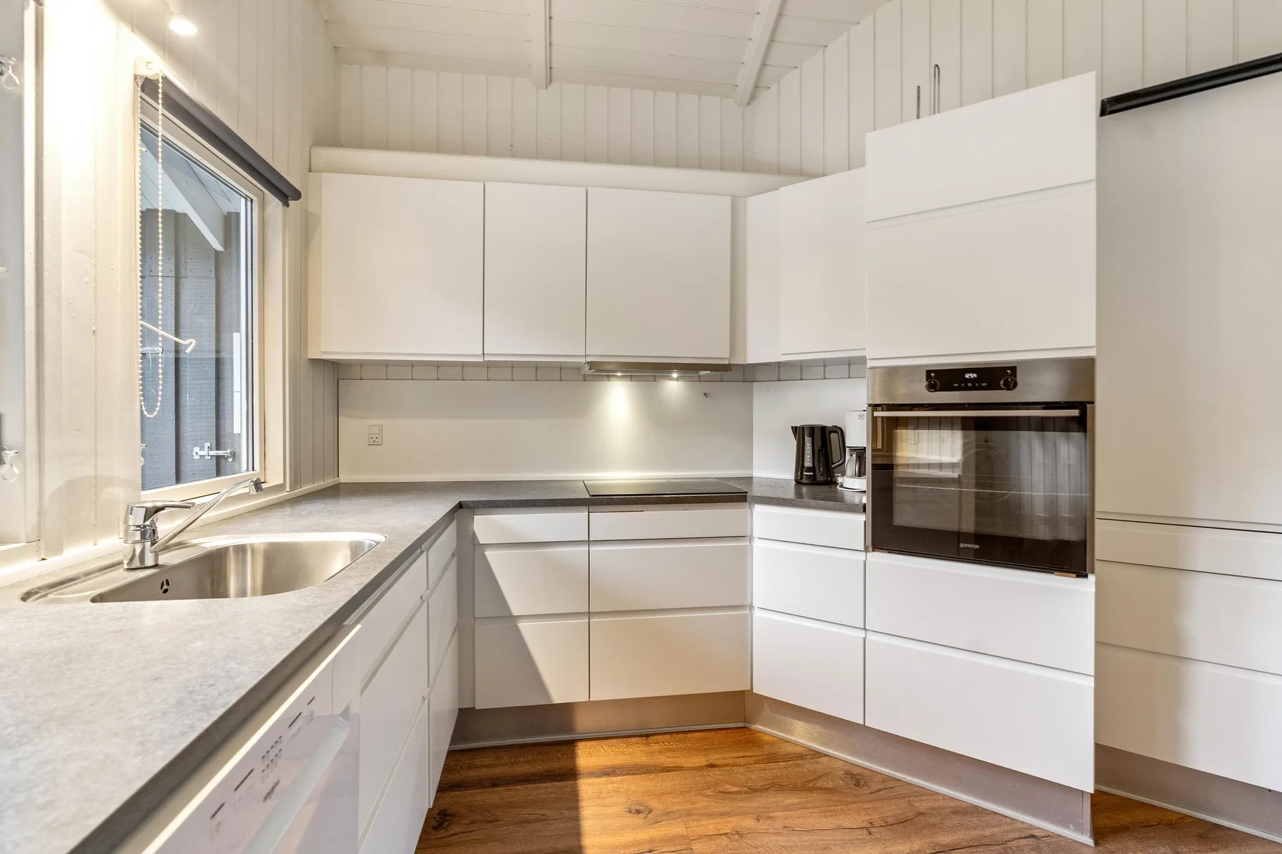 Una cocina luminosa con armarios blancos, una encimera y un horno integrado.