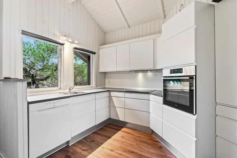 Una cocina blanca y luminosa con horno, encimera y grandes ventanas.
