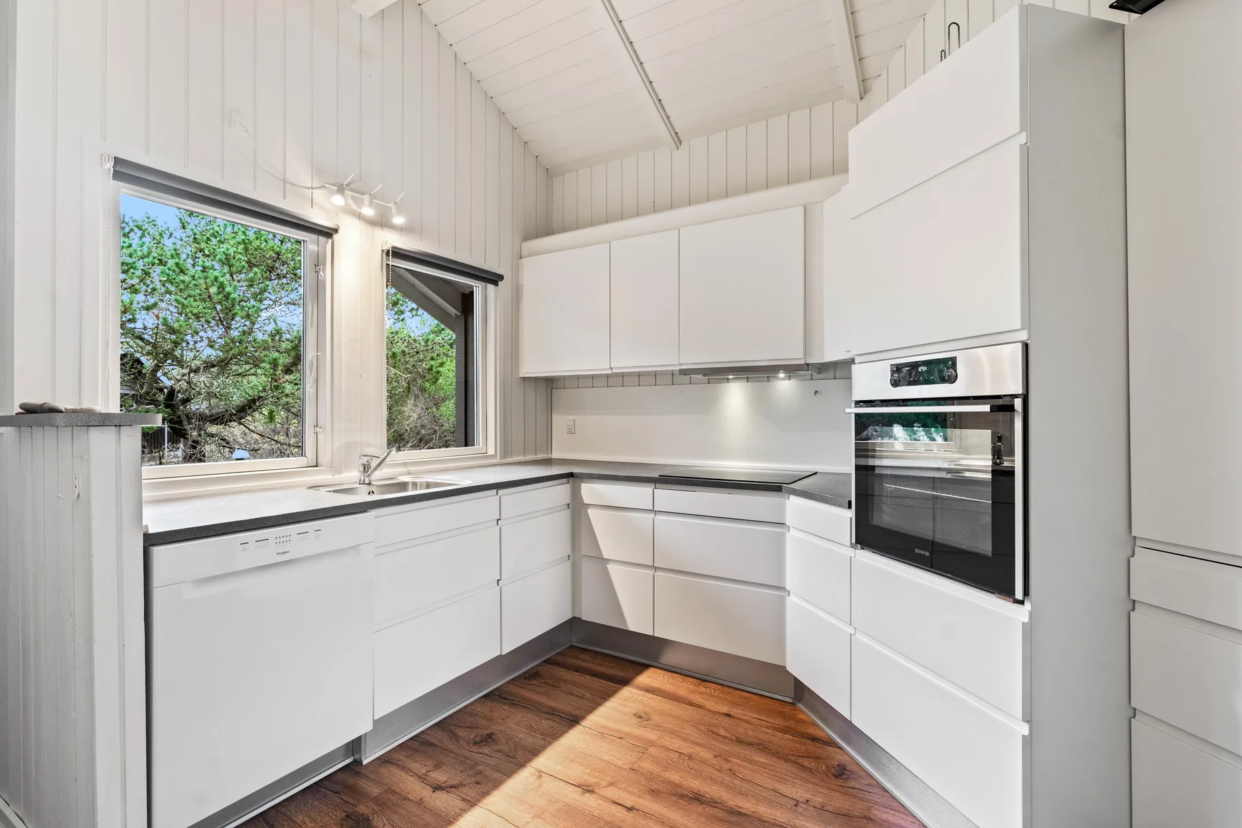 Una cocina luminosa con gabinetes blancos, un horno y ventanas con vista a los árboles.