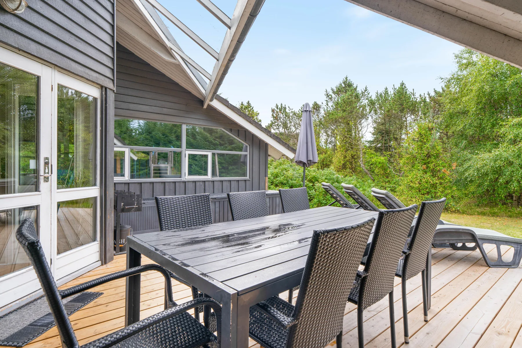 Una terraza de madera con asientos al aire libre y una mesa grande junto a la casa.