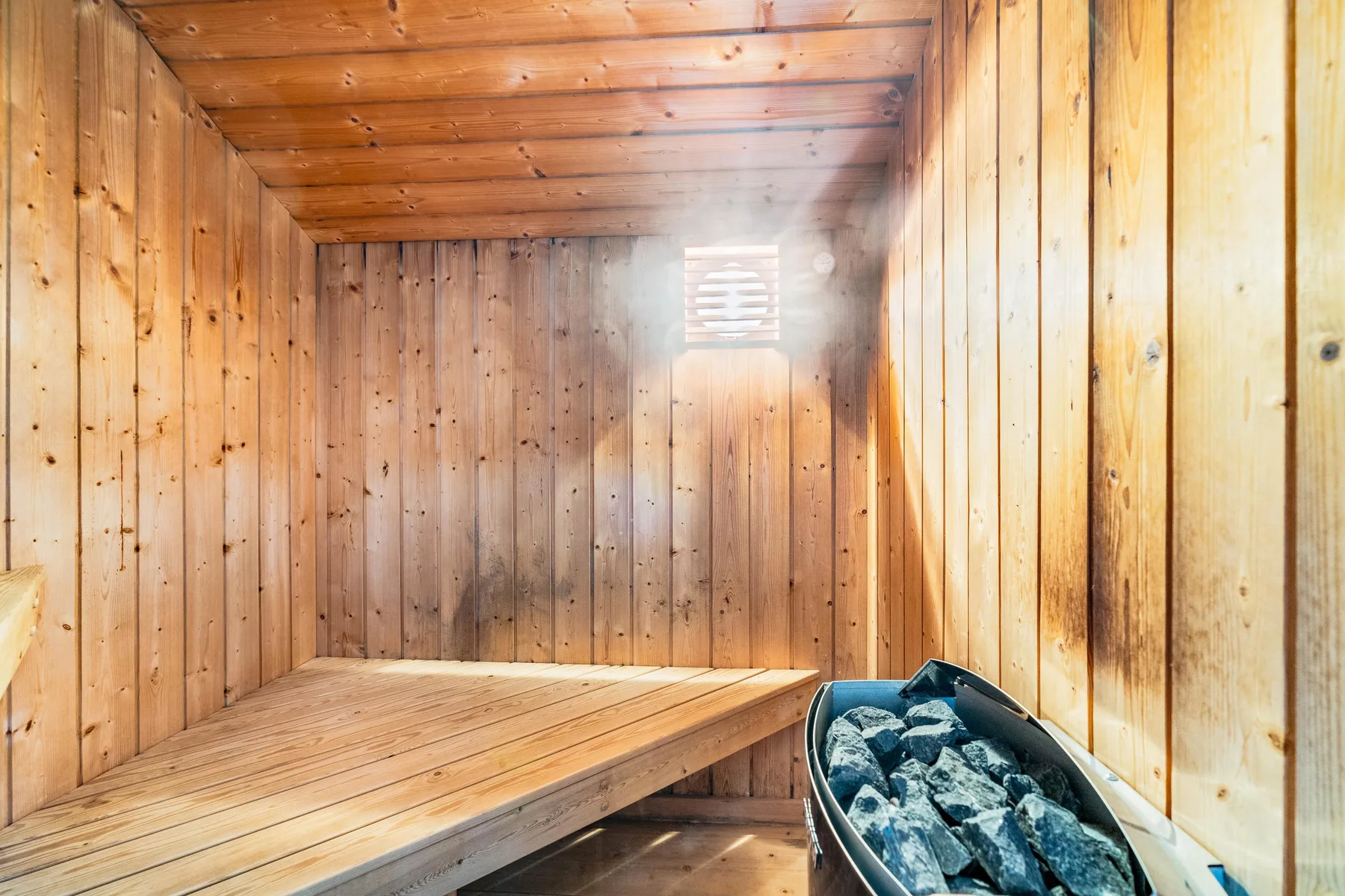 Una sauna de madera con un banco elevado y un recipiente con piedras.