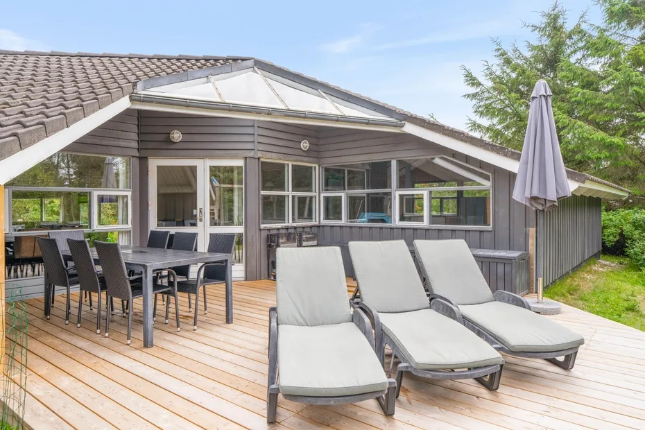 Una terraza de madera con asientos al aire libre y una mesa de comedor junto a una casa moderna.
