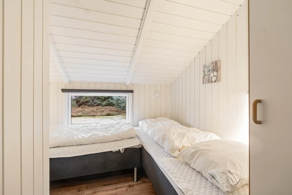 Un dormitorio compacto con dos camas bajo un techo inclinado con paneles.