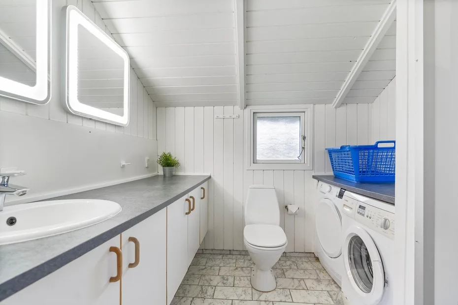 Un baño y cuarto de lavandería compacto con inodoro, lavabo y lavadora.
