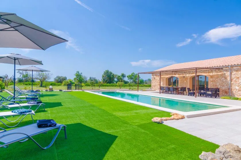 An outdoor swimming pool beside a covered patio, with loungers on the lawn.