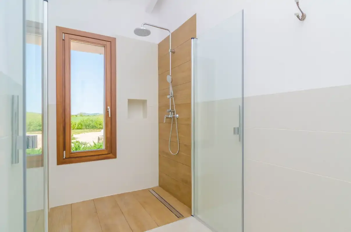 A bathroom with a glass shower and a window overlooking greenery.