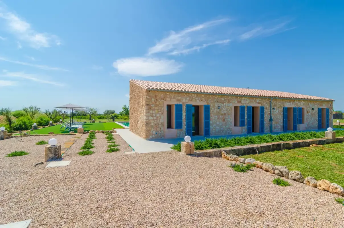 A stone building stands beside a gravel courtyard and landscaped garden.