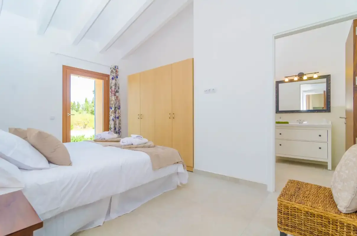 A bright bedroom with a bed beside a wooden wardrobe and an open doorway.