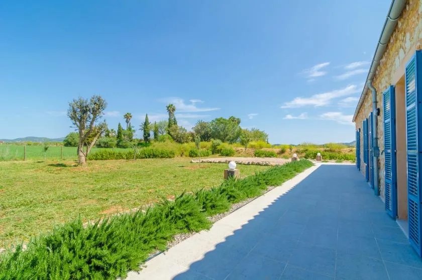 A paved outdoor terrace runs alongside a stone building, overlooking green fields.